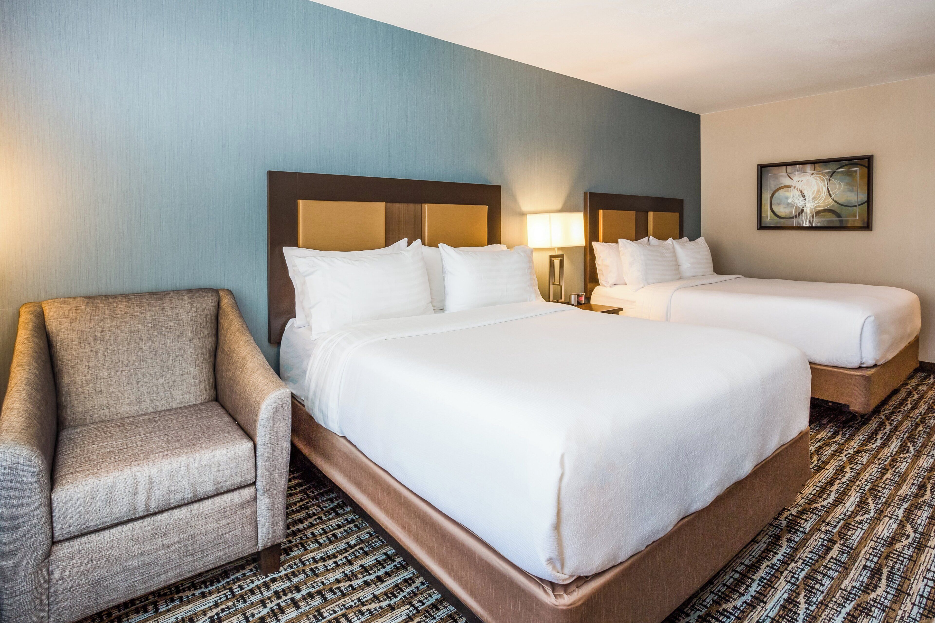 Habitación de hotel con dos camas, una silla y un cuadro en la pared.