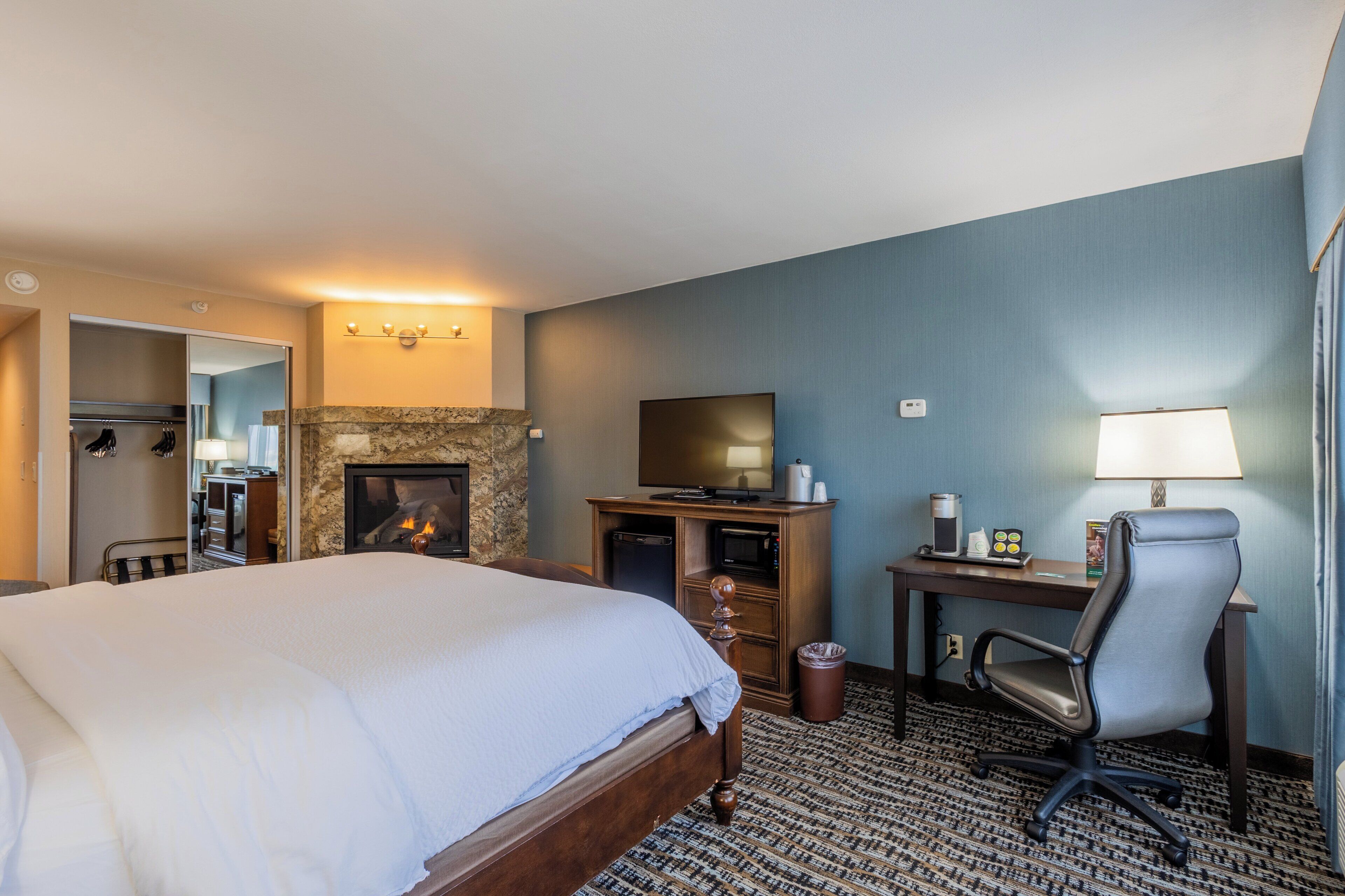 Ein Hotelzimmer mit einem großen Bett, einem Schreibtisch mit Computer, einem Fernseher und einem Kamin.