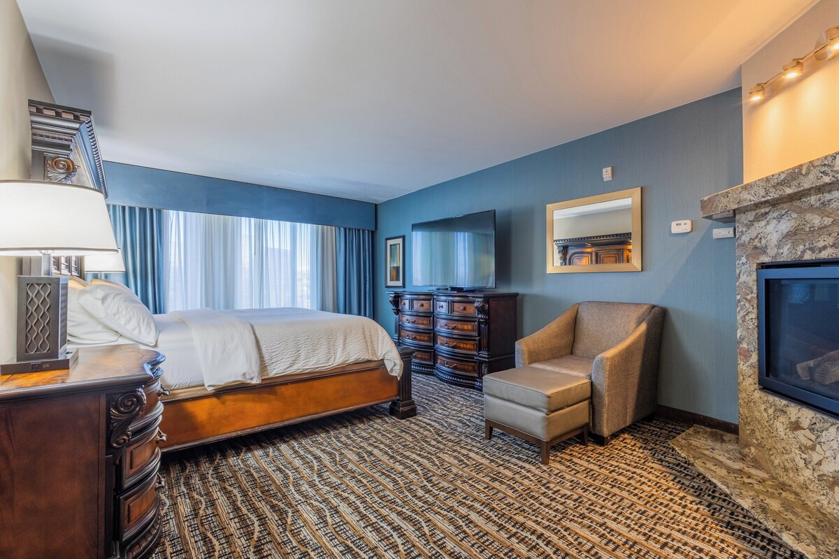 Een hotelkamer met een groot bed, een dressoir, een stoel, een televisie en een open haard.