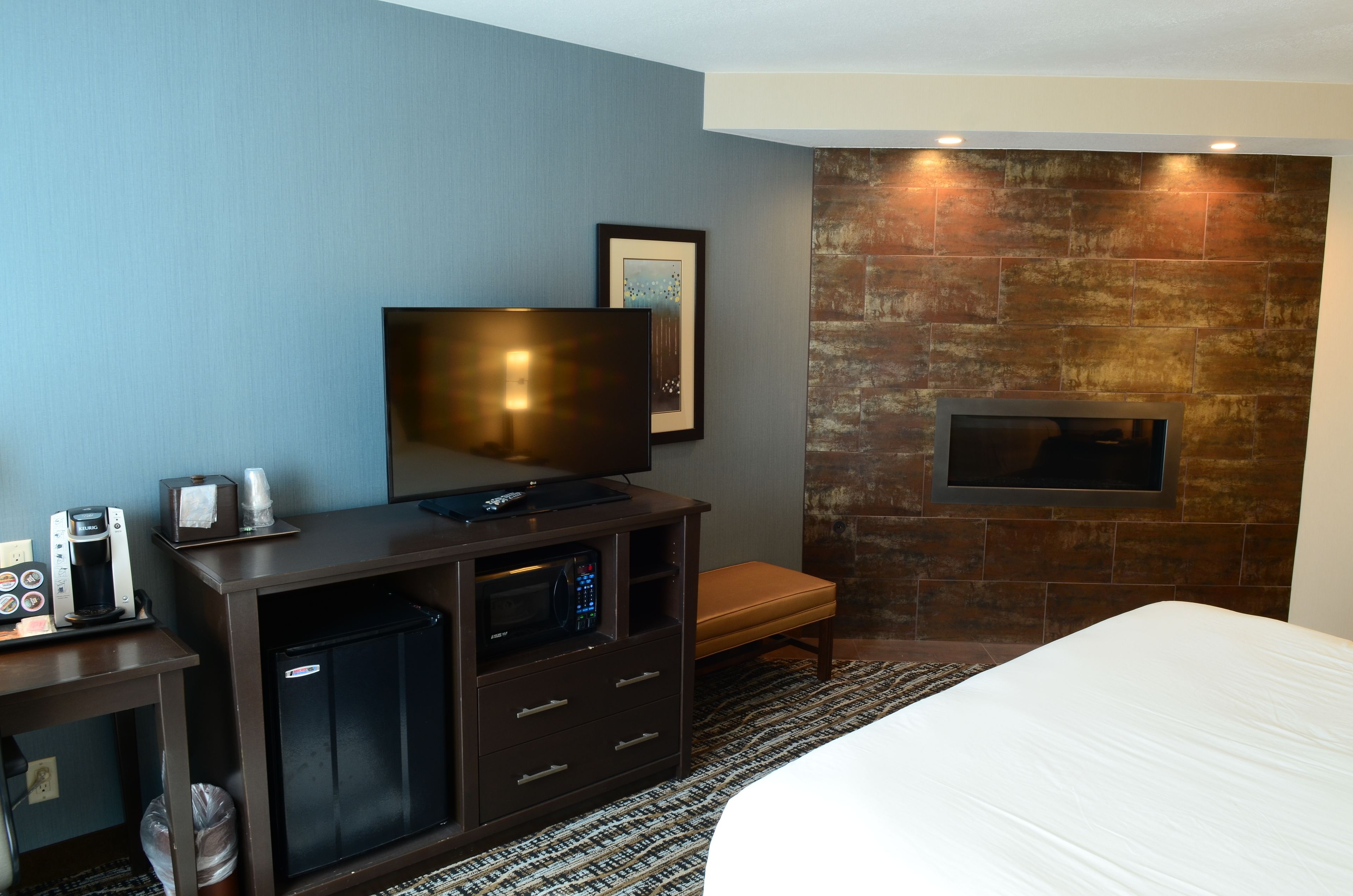 Ein Hotelzimmer mit einem Bett, einem Fernseher auf einer Holzkommode, einer Kaffeemaschine, einer Mikrowelle und einem kleinen Kühlschrank.