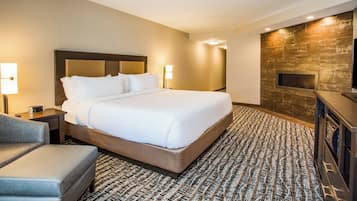 A hotel room with a large bed, a flat-screen TV, a sofa, and a fireplace.