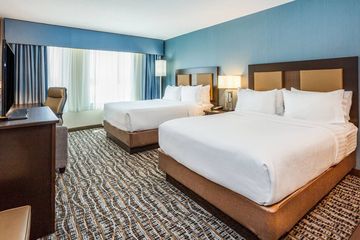 A hotel room with two beds, a desk, and a TV.