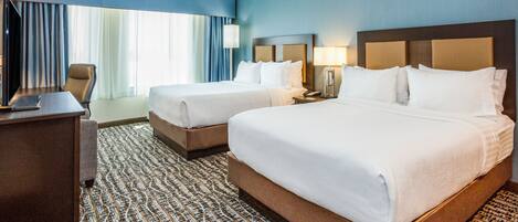 A hotel room with two beds, a desk, and a TV.