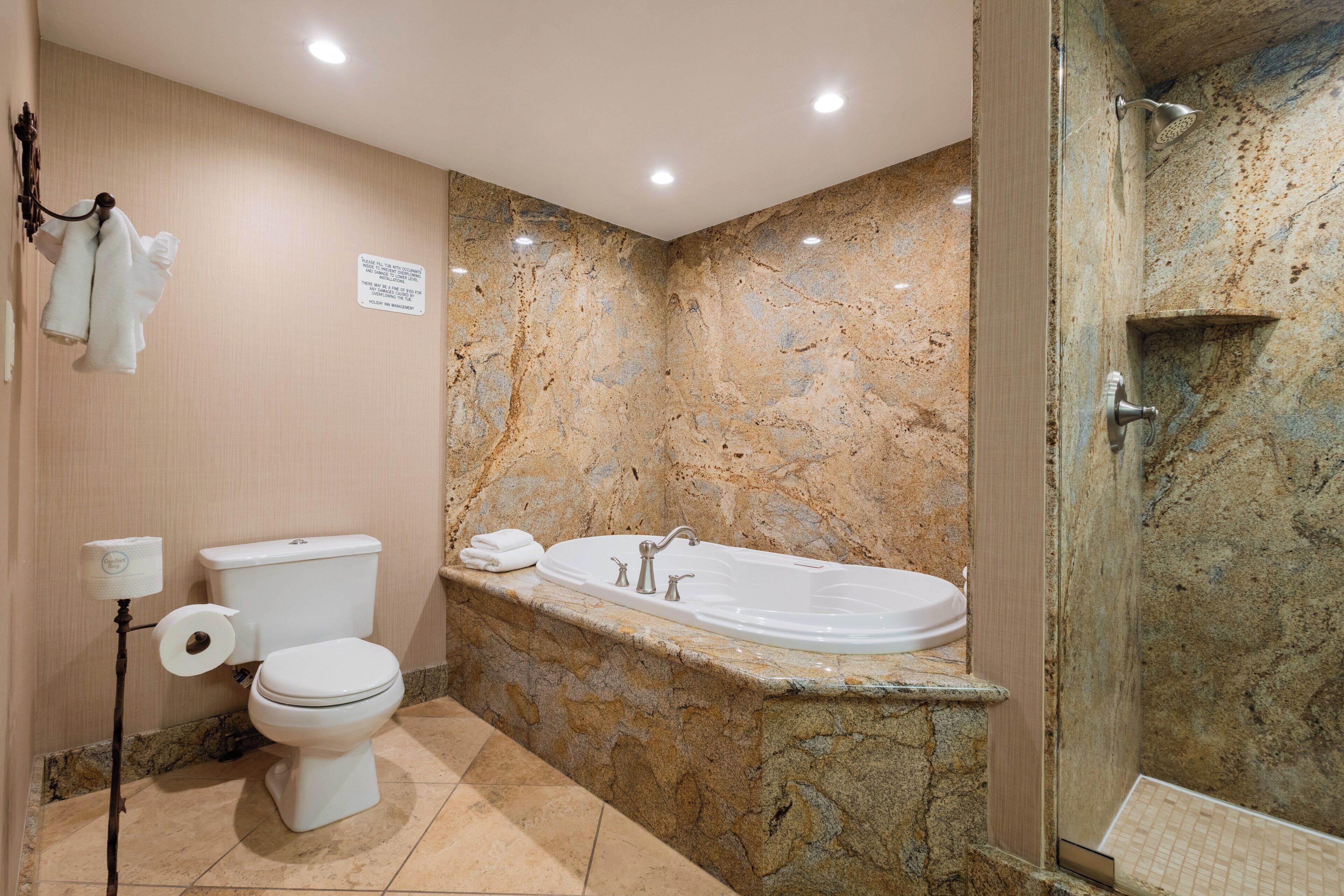 A bathroom with a marble wall, a bathtub, a toilet, and a shower.