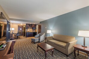 Hotelkamer met een zithoek, inclusief een bank, fauteuils, een salontafel en een bureau met een computer. Er is ook een keuken met een magnetron en een koelkast.