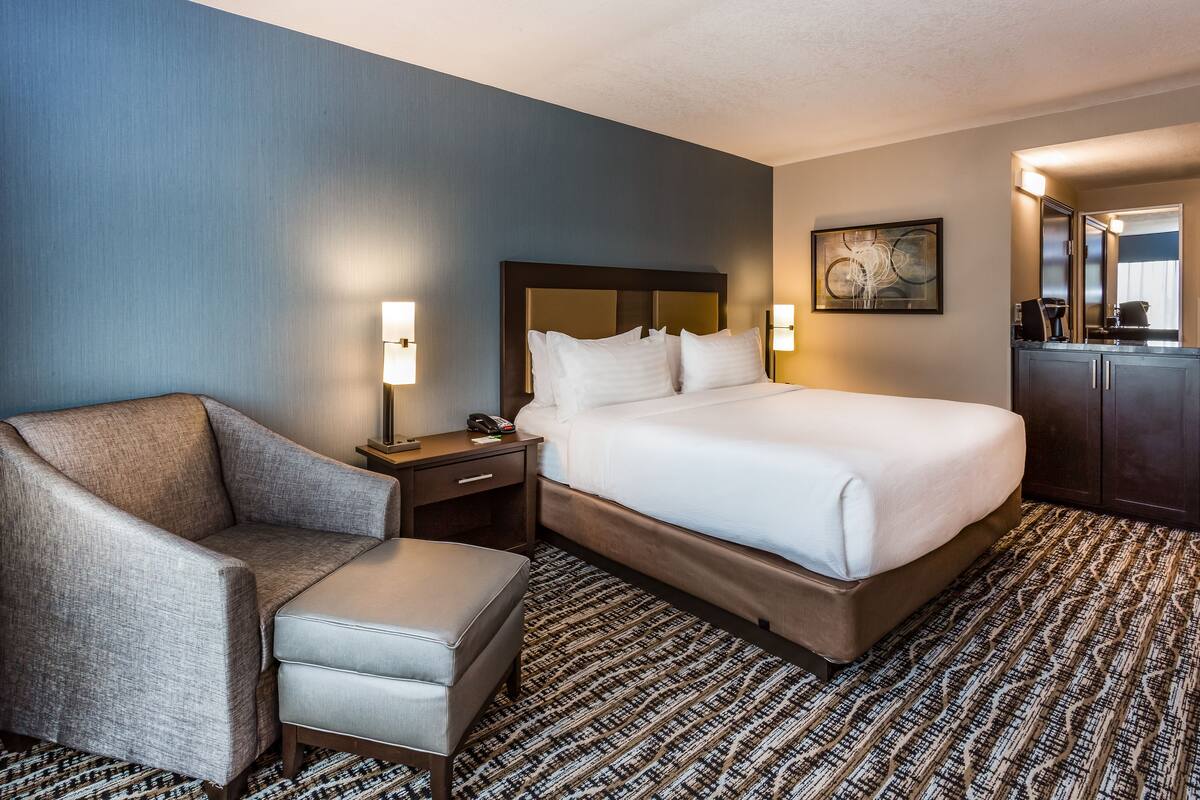 A hotel room with a bed, a chair, a desk, and a dresser.