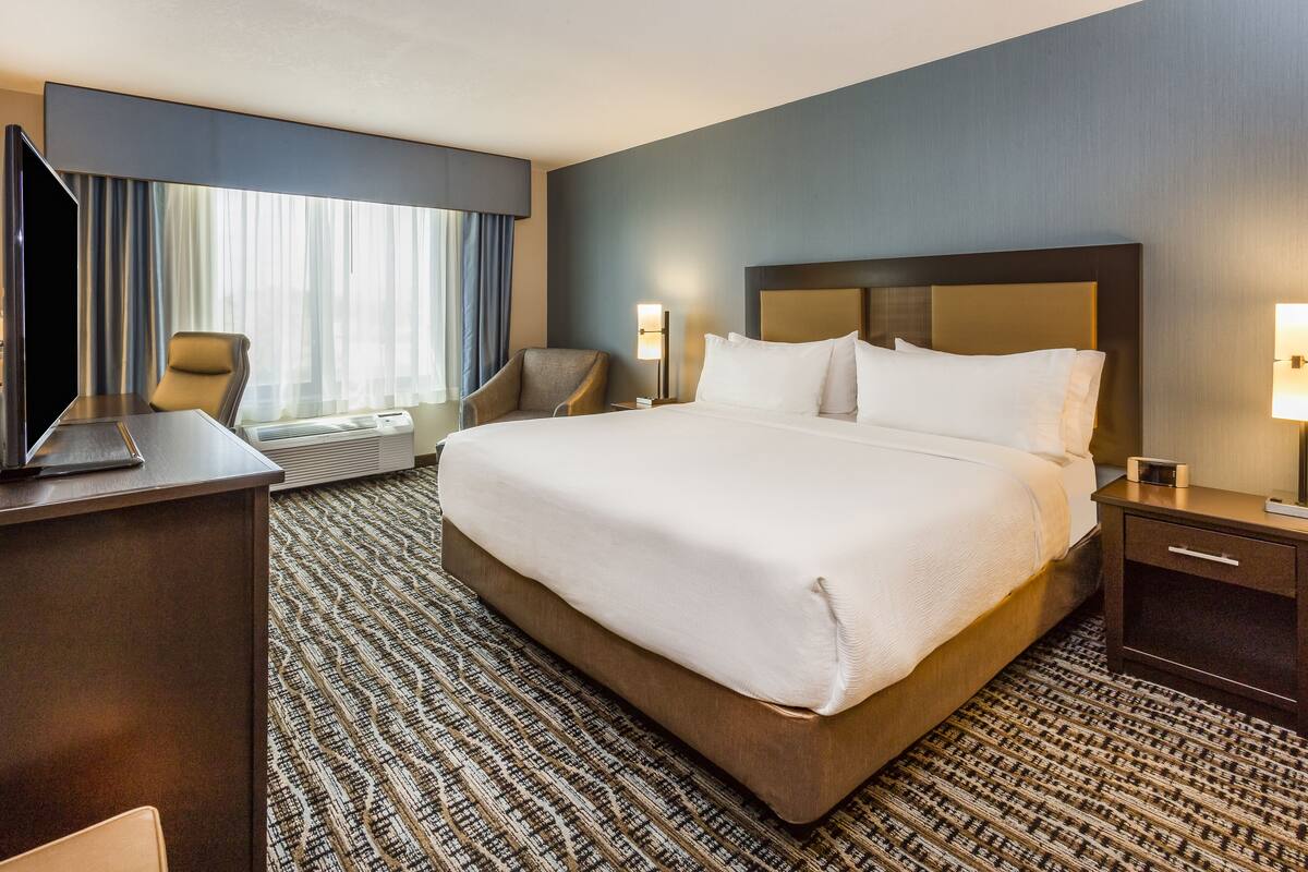 A hotel room with a large bed, a desk with a computer, a chair, and a TV.