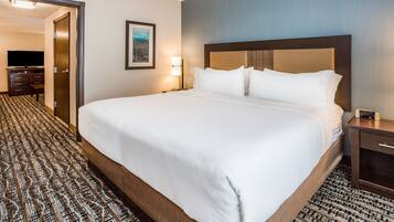 A hotel room with a large bed, a desk, a chair, a television, and a framed picture on the wall.