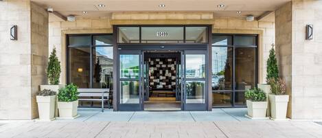 A hotel entrance with a modern design, featuring a glass facade, a number sign above the doors, and potted plants on either side.