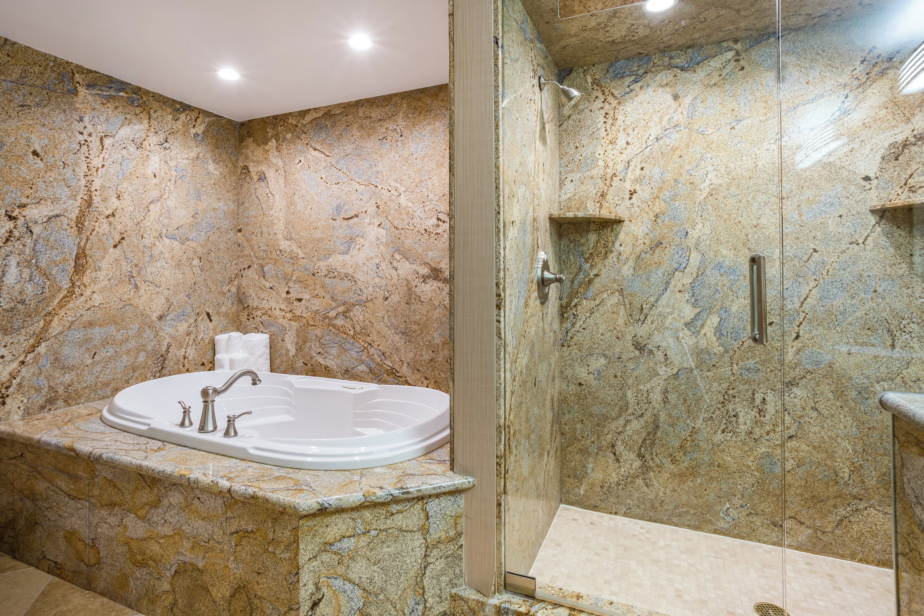 Une salle de bain avec un mur en marbre, une baignoire sur pieds et un espace douche séparé.