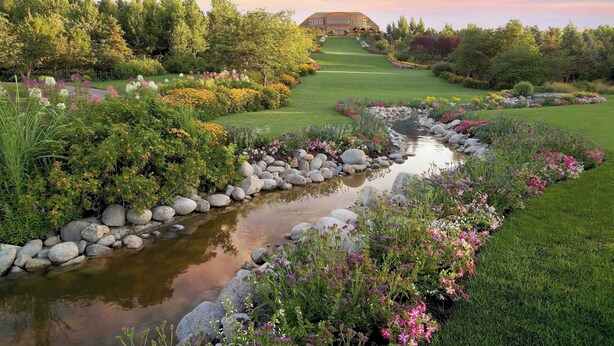 A golf course with a pond, surrounded by lush greenery and flowering plants.