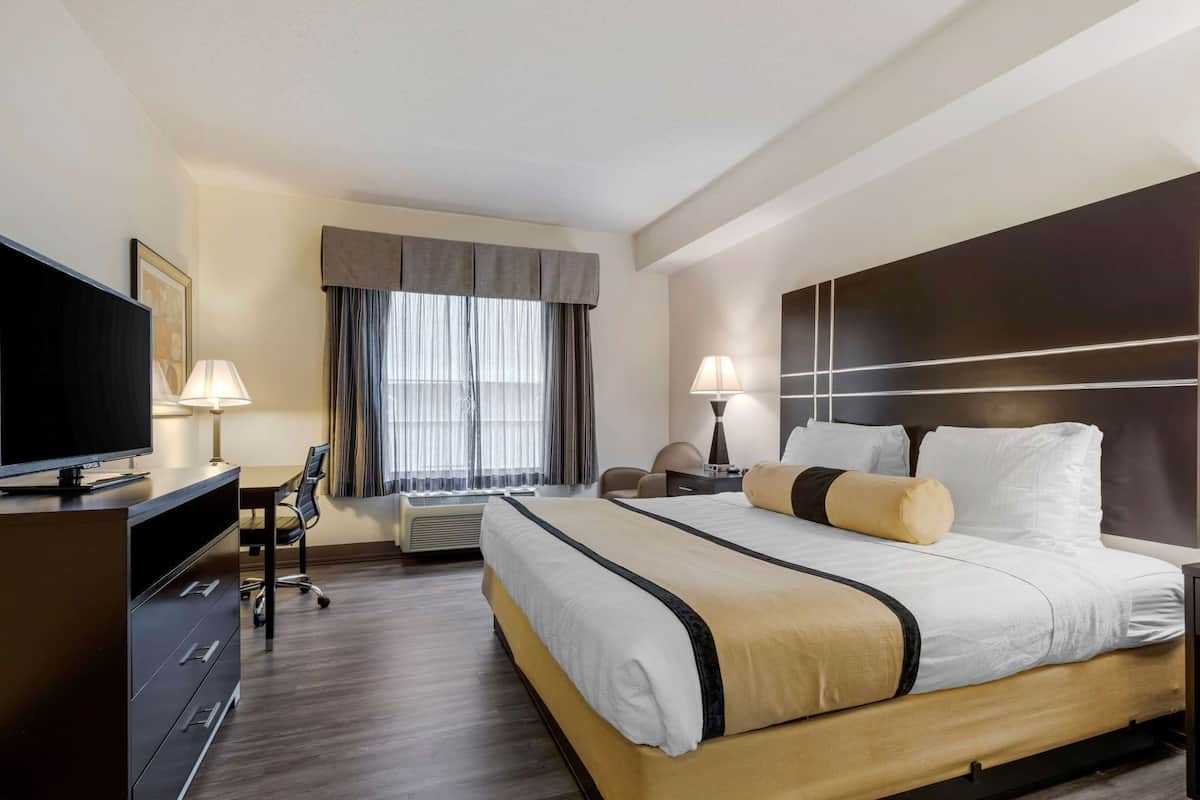 A hotel room with a bed, TV, desk, chair, and a window with curtains.