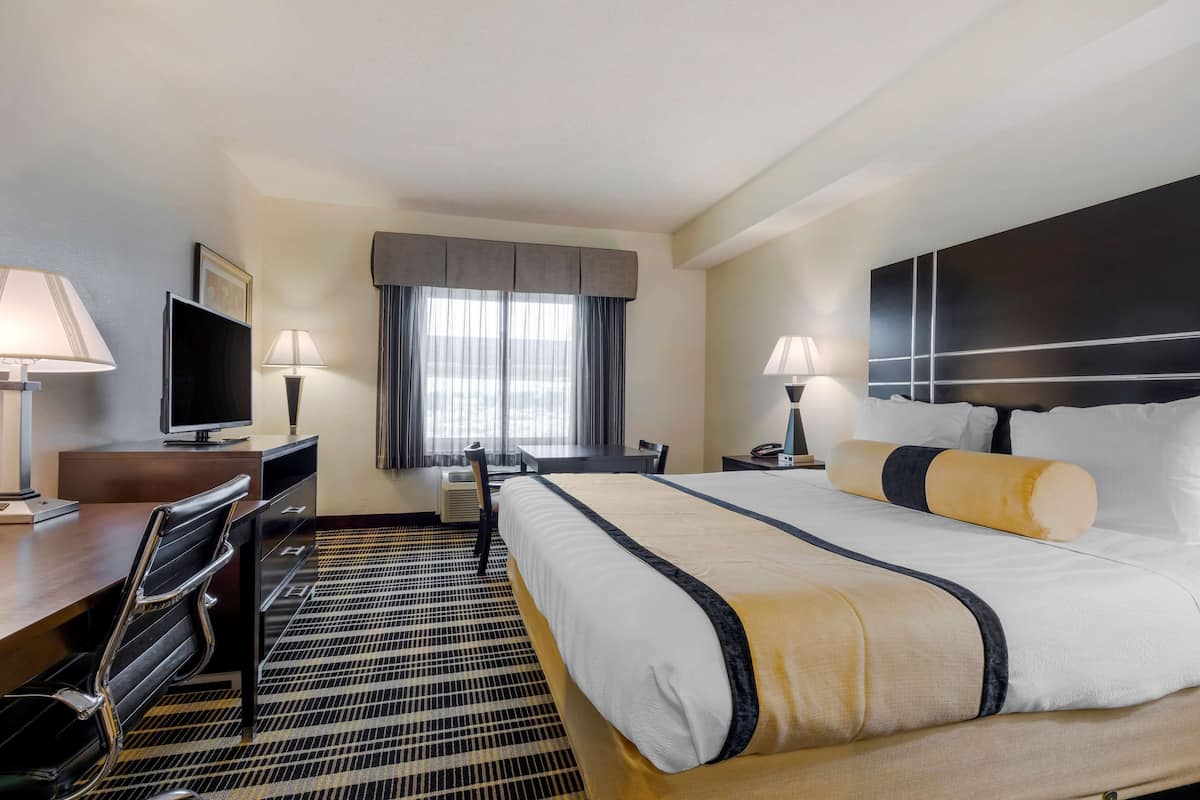 A hotel room with a bed, desk, chair, TV, and lamps.