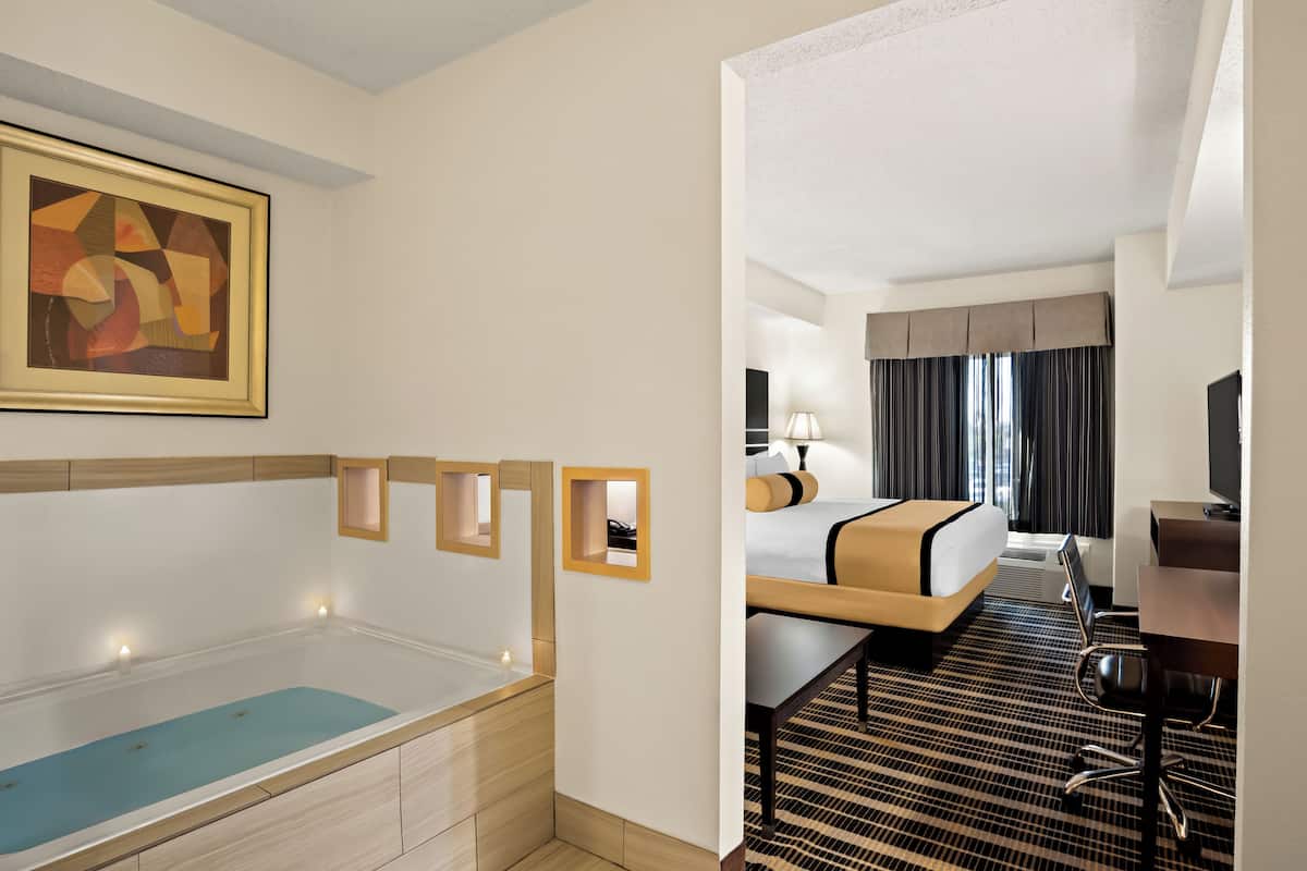 A hotel room with a bathtub, a bed, a desk, and a television.