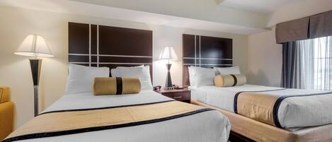 A hotel room with two beds, each with a headboard, bedside tables, lamps, and a window with curtains.