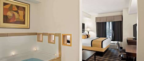 A hotel room with a bathtub, a bed, a desk, and a television.