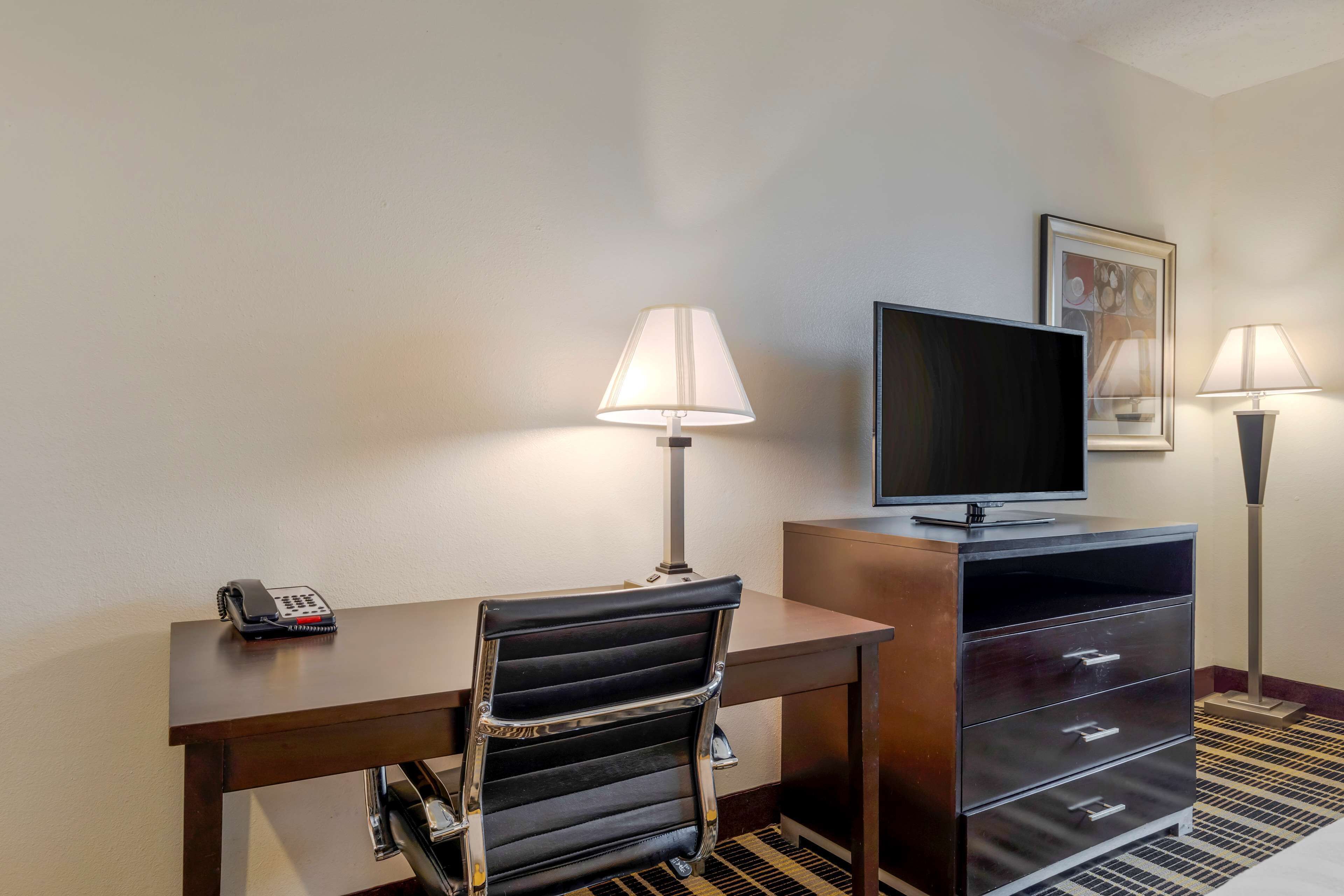 A hotel room with a desk, a chair, a television, a telephone, and two lamps.