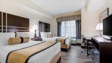 A hotel room with two beds, a desk, a chair, a TV, and a window with curtains.