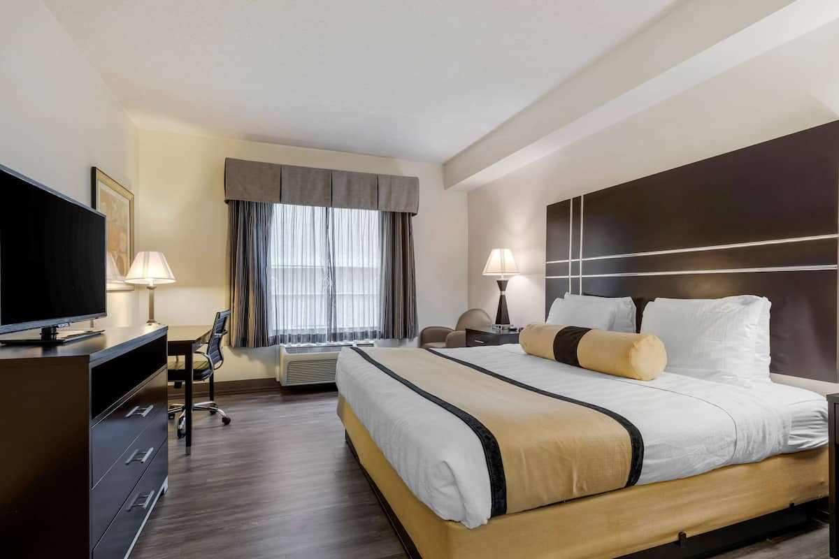 A hotel room with a large bed, a desk, a chair, a television, and a window with curtains.