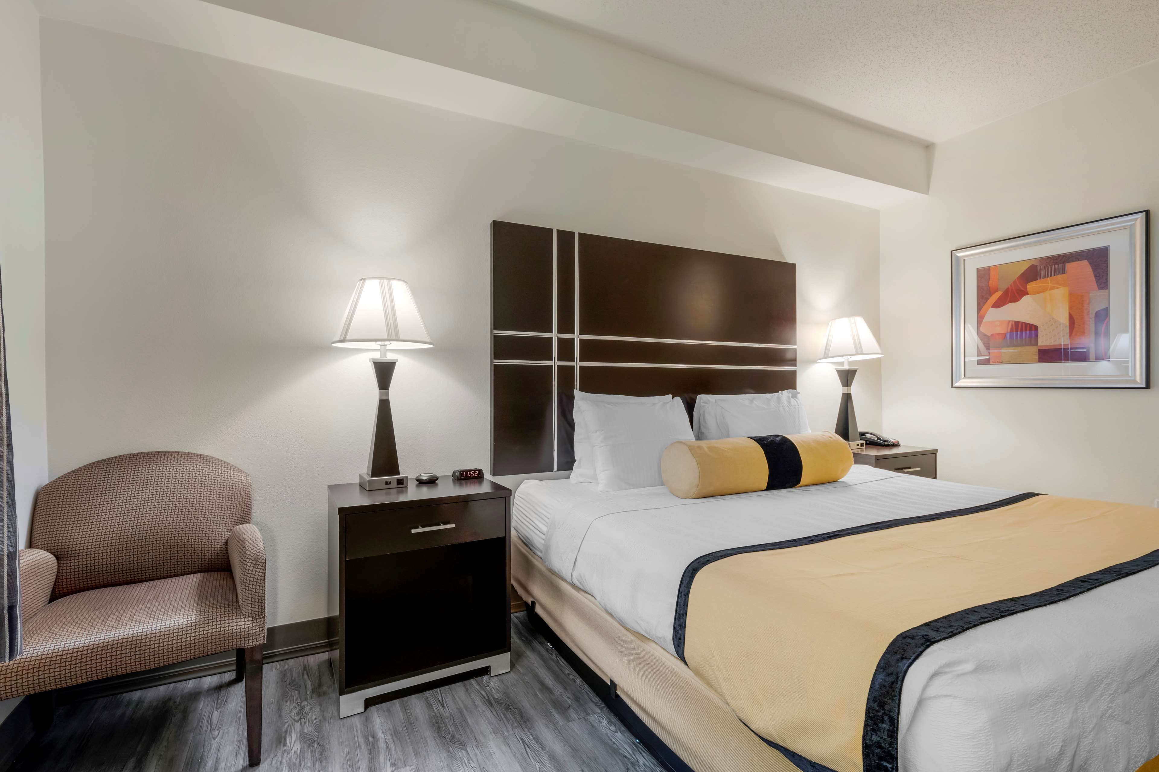 Une chambre d’hôtel comprenant un lit, deux tables de chevet avec des lampes, une chaise et une œuvre d’art accrochée au mur.