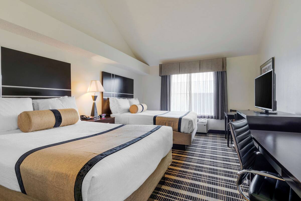 A hotel room with two beds, a desk, a TV, and a window with curtains.