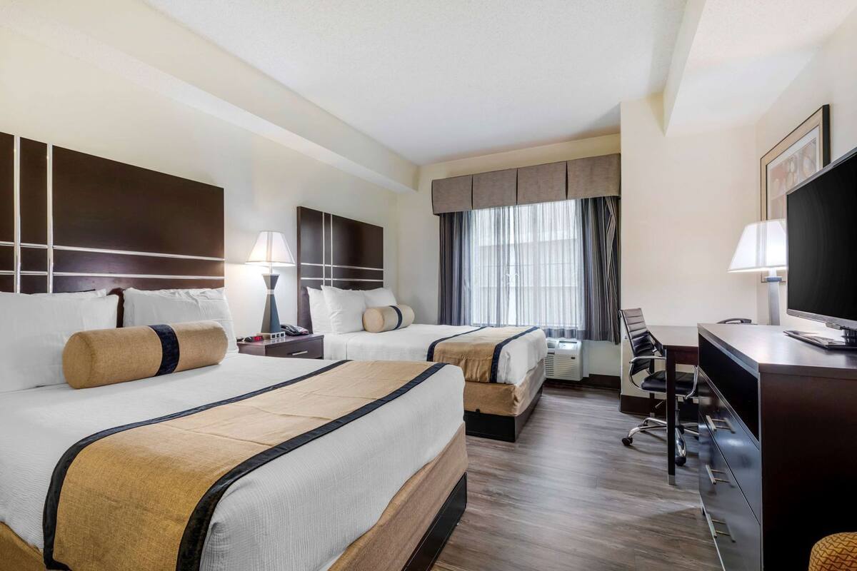 A hotel room with two beds, a desk, a chair, a television, and a window with curtains.