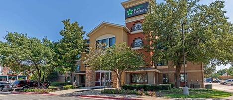 A hotel with a sign for Extended Stay America, featuring a brick facade, multiple balconies, and a landscaped front yard.