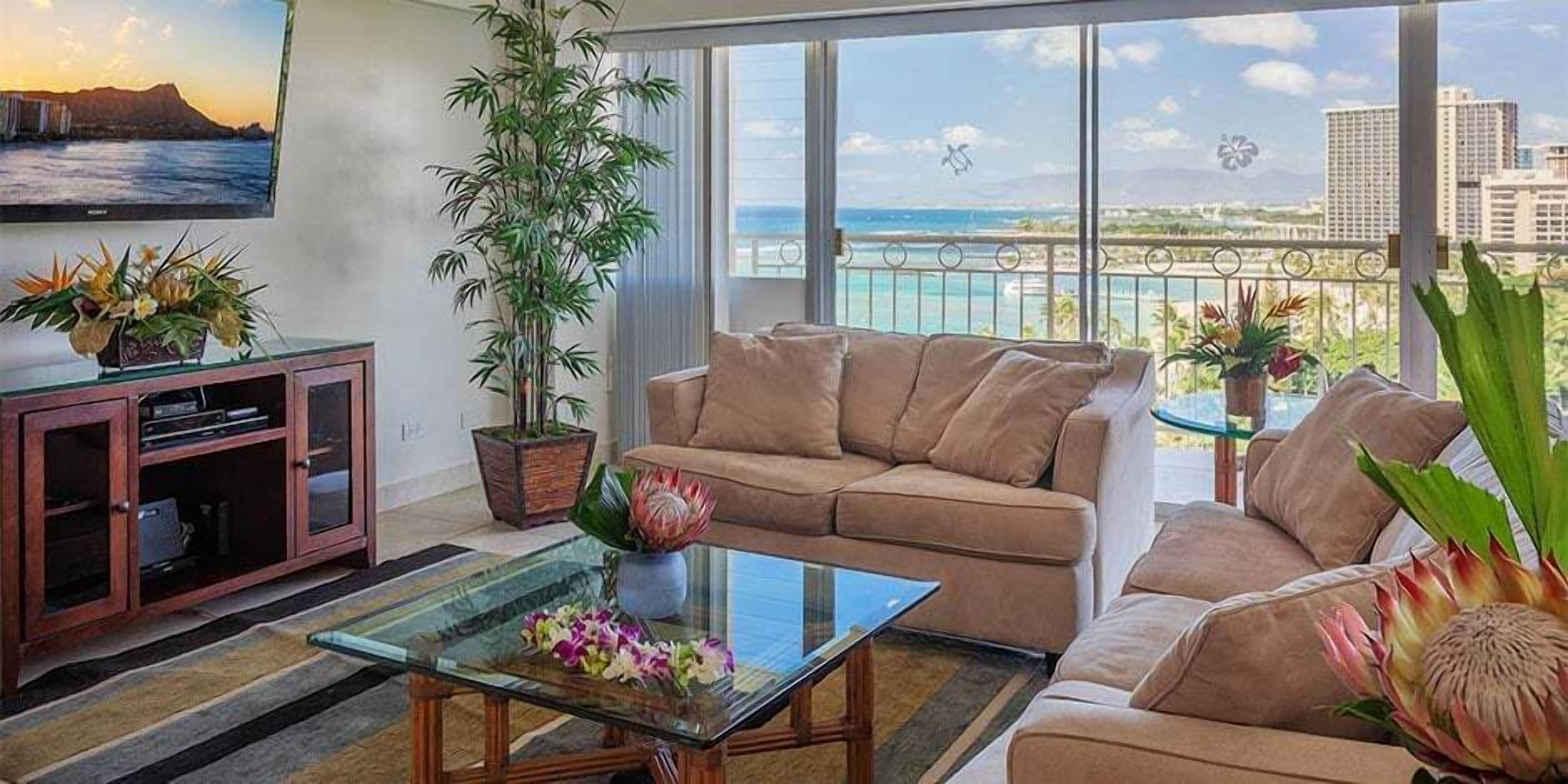 A living room with a sofa, a glass coffee table, a TV, and a large window with a view of the city.