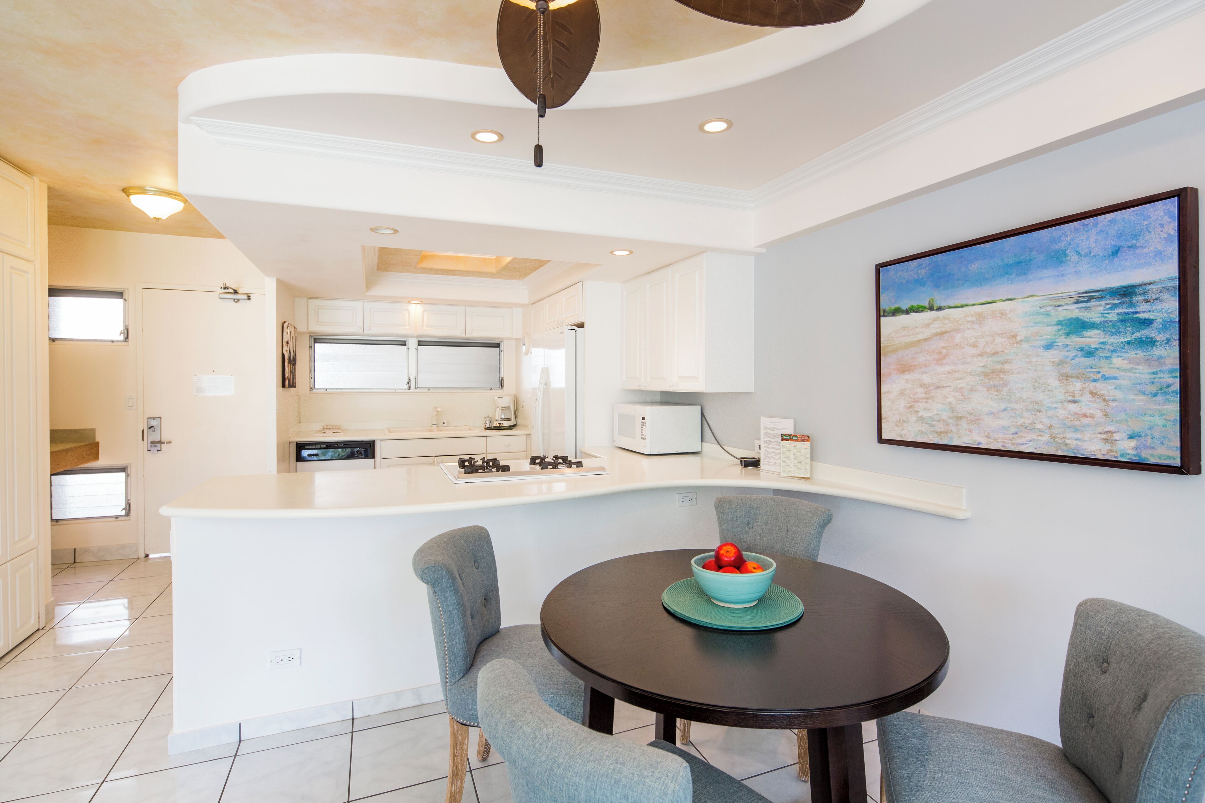 A modern kitchen with white cabinets, a central island, and a dining area with a round table and chairs.