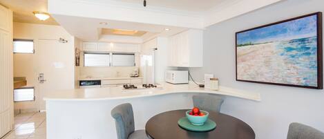 Een moderne keuken met witte kasten, een centraal eiland en een eetgedeelte met een ronde tafel en stoelen.