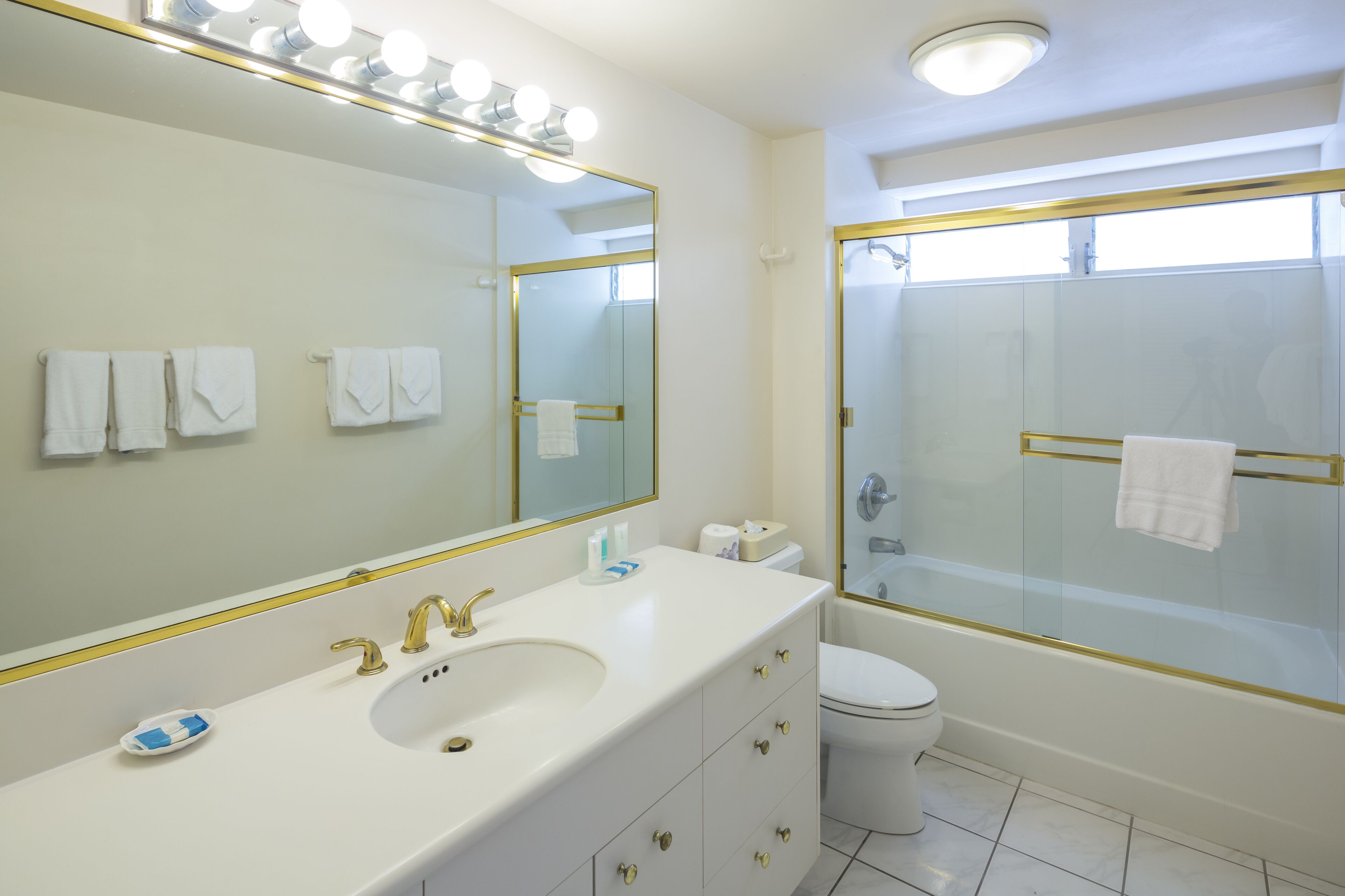 Een badkamer met een witte wastafel, gouden details, een grote spiegel en een douche met glazen wanden.