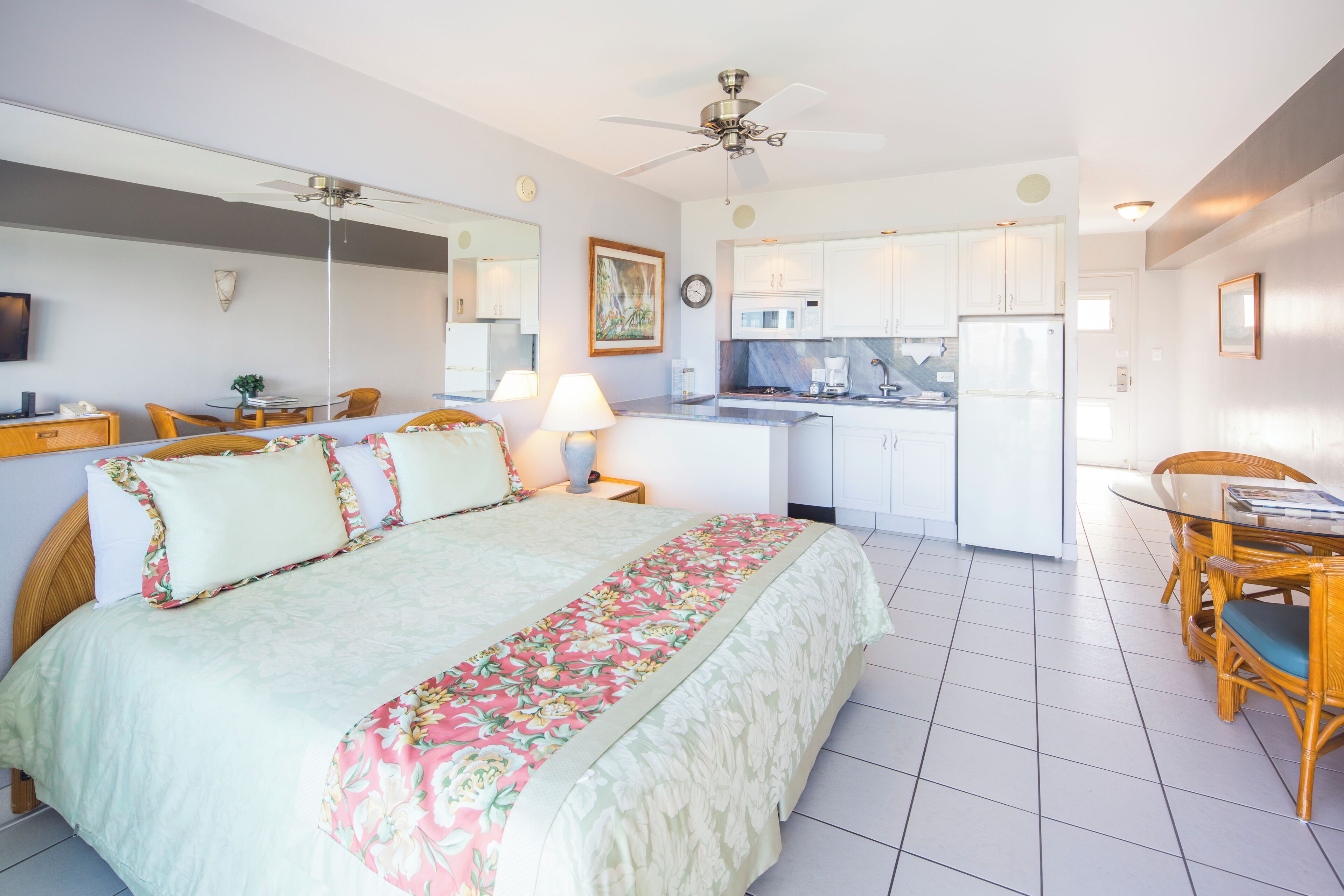 A hotel room with a bed, a dining table, a kitchen area, and a ceiling fan.