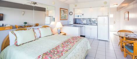A hotel room with a bed, a dining table, a kitchen area, and a ceiling fan.