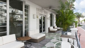 A modern outdoor seating area with white sofas, a wooden table, and a checkered floor. - The Shepley South Beach Hotel (Miami Beach)