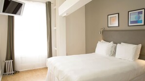 Une chambre d’hôtel avec un grand lit, un téléviseur à écran plat fixé au mur et un radiateur près de la fenêtre.