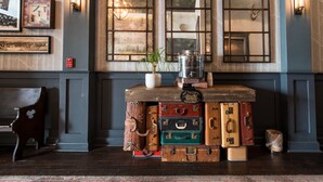 Un espace bar avec un comptoir en bois, des valises anciennes empilées servant de support, une machine à café et une plante en pot.