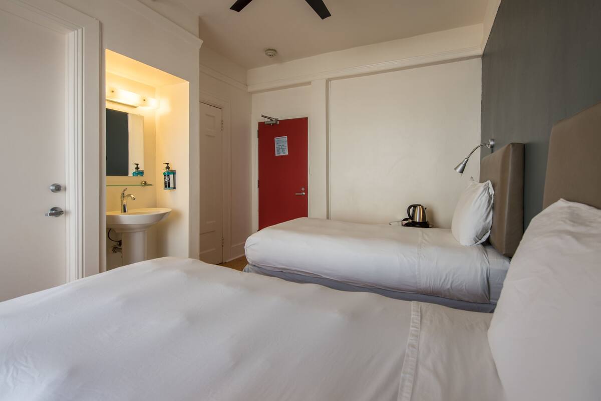 Una habitación de hotel con dos camas, una puerta roja, un lavamanos y un espejo.