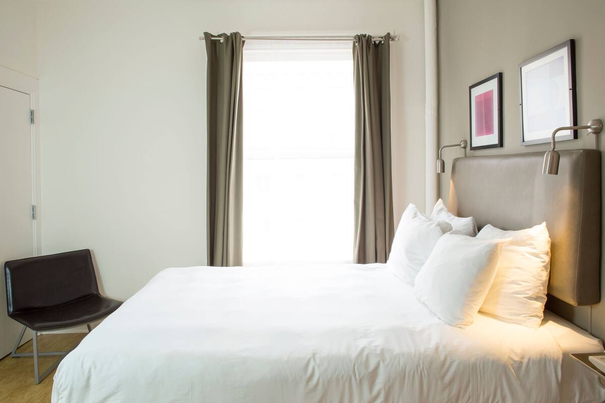 Una habitación de hotel con cama, una silla y ventana con cortinas.