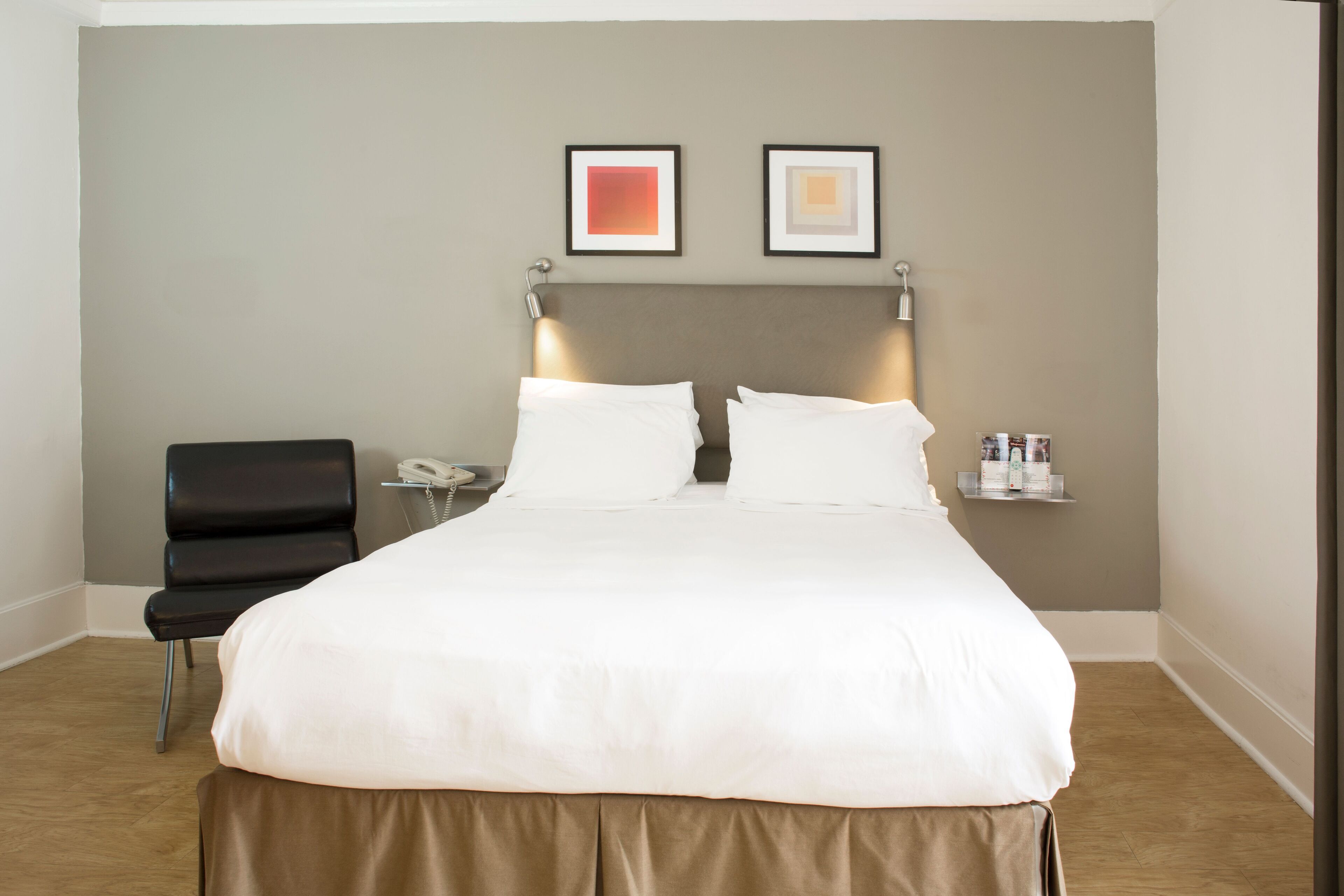 A hotel room with a large bed, a chair, a bedside table with a lamp, and two framed pictures on the wall.