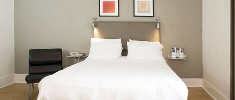 A hotel room with a large bed, a chair, a bedside table with a lamp, and two framed pictures on the wall.