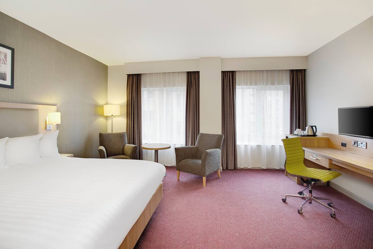 Habitación de hotel con una cama grande, dos sillones, un escritorio con una silla, un televisor y una mesita.