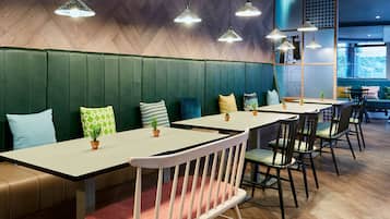 A restaurant with booths and tables, green upholstered seating, hanging pendant lights, and a herringbone wood wall.