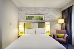 A hotel room with a large bed, two bedside lamps, a chair, and a framed picture on the wall.