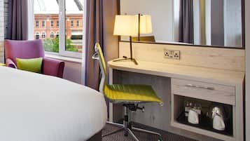 Habitación de hotel con cama, escritorio con lámpara, silla y zapatero.