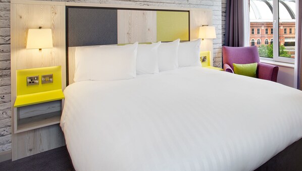 Habitación de hotel con una cama grande, dos lámparas de noche, cabecera de madera y vista a un edificio a través de la ventana.