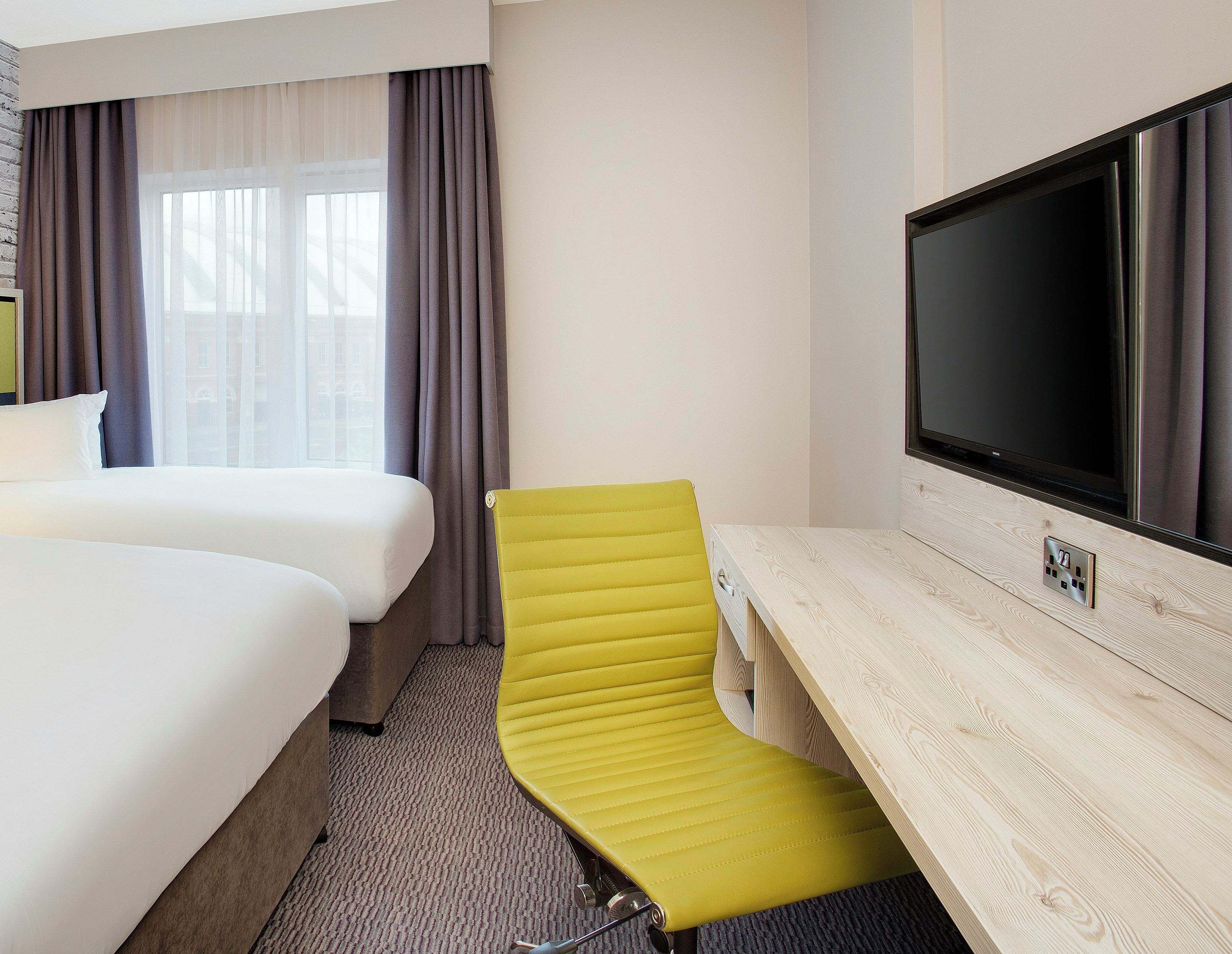A hotel room with a bed, a desk, a television, and a window with curtains.