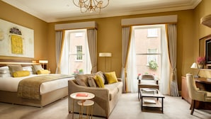 A hotel room with a bed, a sofa, a desk, and a chair. There are curtains on the windows, a lamp, and a painting on the wall. - Trinity Townhouse Hotel (Dublin)