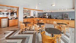 A modern kitchen with wooden cabinets, a central island, and a seating area with round tables and chairs.