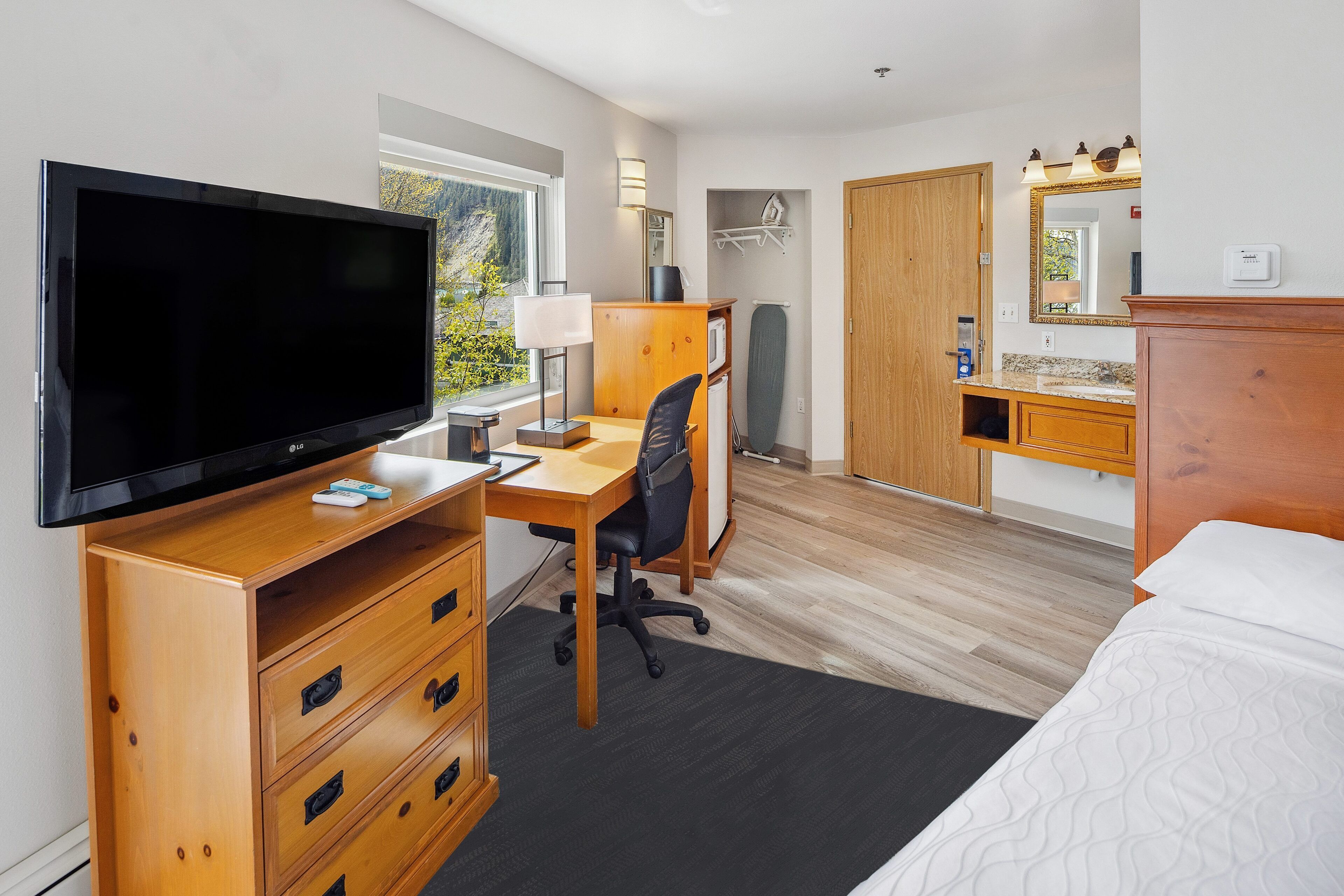 A hotel room with a TV, desk, chair, and bed.