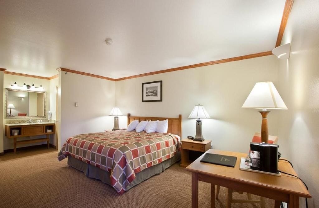 A hotel room with a bed, bedside lamps, a desk, a mirror, and a framed picture on the wall.